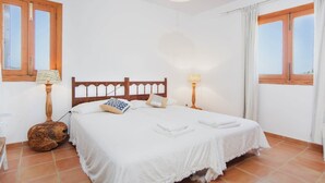 A bedroom with a large bed, two bedside lamps, a wooden headboard, and a window with curtains.