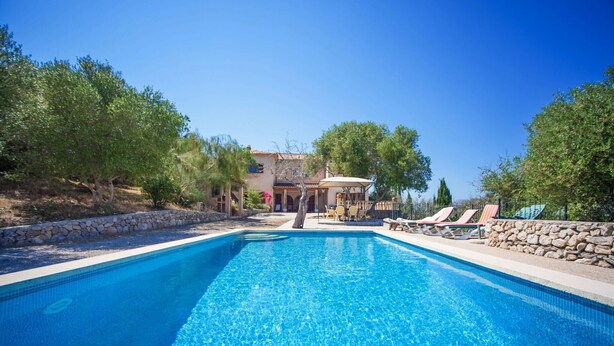 A rectangular swimming pool with clear blue water, surrounded by stone walls and trees.