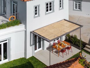 A modern house with a covered patio, a dining table with chairs, and a small garden area. - Beautiful villa with rooftop pool | CarmHim (Calheta)