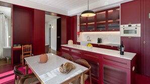 A modern kitchen with red cabinetry, a marble countertop, and a dining area with a table and chairs. - Beautiful villa with rooftop pool | CarmHim (Calheta)
