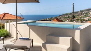 A pool with steps leading up to it, a table with chairs, and an umbrella. - Beautiful villa with rooftop pool | CarmHim (Calheta)