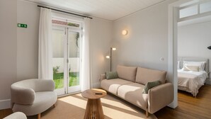 A modern living room with a sofa, armchairs, a round wooden coffee table, and a sliding glass door leading to a balcony. - Beautiful villa with rooftop pool | CarmHim (Calheta)