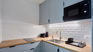 A modern kitchen with white subway tiles, a wooden countertop, a stainless steel sink, and a black microwave. - Magnificent Apartment Etoile Hoche Saint Honore (Paris)