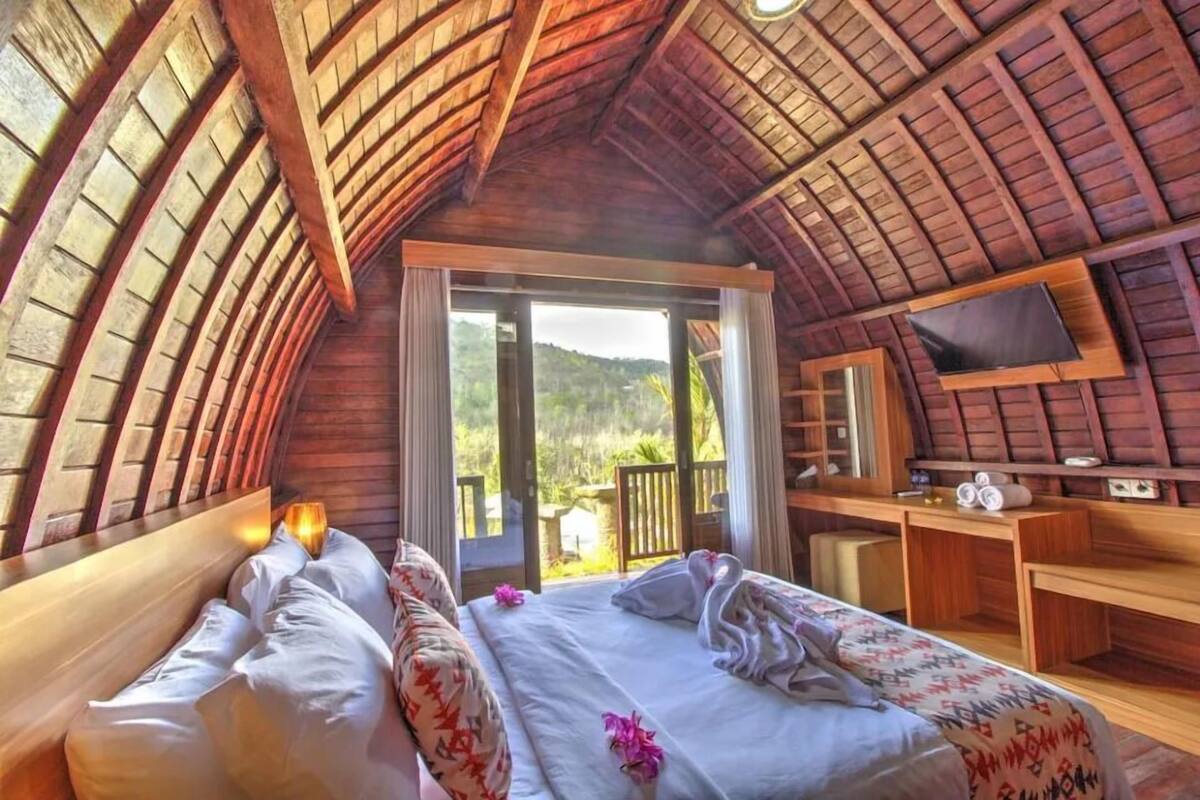 Un'accogliente camera da letto con tetto in legno, due letti, una TV e un balcone con vista panoramica.
