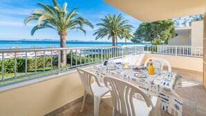 A balcony with a table set for breakfast, overlooking a beach with palm trees and the sea. - Bon Estar - Apartment In Port D'alcúdia (Port D'alcúdia, Illes Balears)