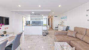 A modern kitchen with white cabinets, a central island, and a dining area with a table and chairs. - Bon Estar - Apartment In Port D'alcúdia (Port D'alcúdia, Illes Balears)