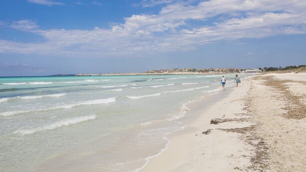 Une plage aux eaux turquoise et limpides, bordée d’un rivage sablonneux.