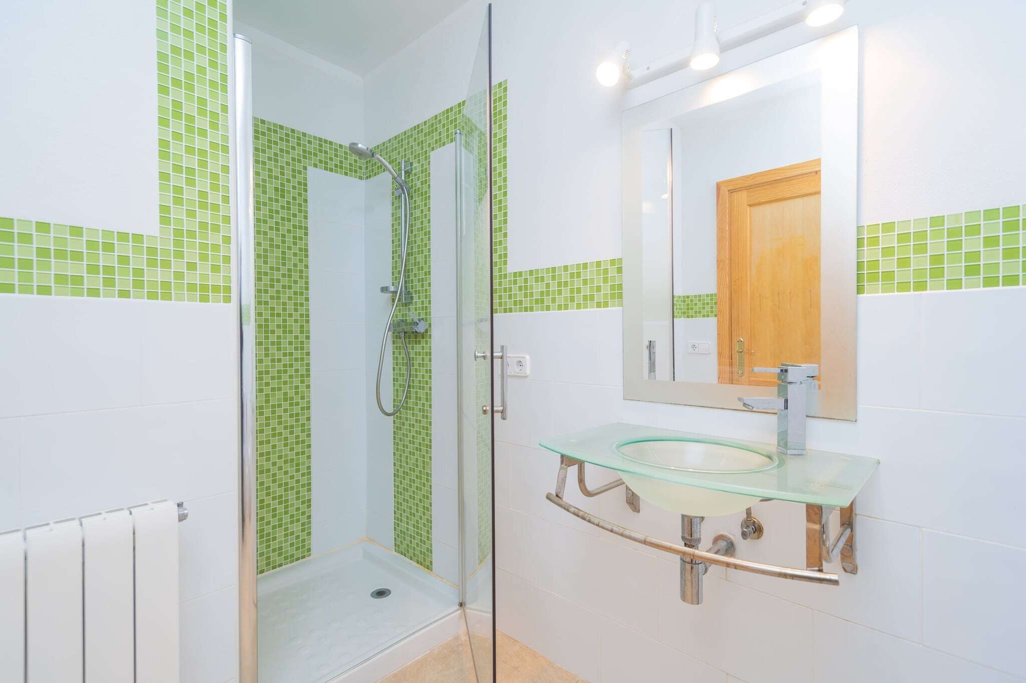 A bathroom with a glass shower enclosure, a glass sink, and a wooden door.