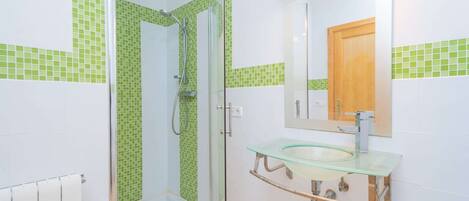 A bathroom with a glass shower enclosure, a glass sink, and a wooden door.