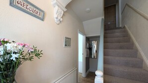 Un corridoio con il cartello 'WELCOME', un termosifone, una scala e una porta che dà su una stanza con un appendiabiti e degli asciugamani.