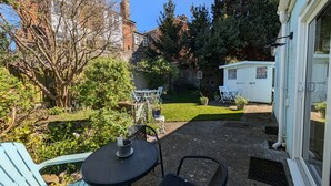 Un patio con posti a sedere all'aperto, un piccolo capanno e un giardino alberato con prato.