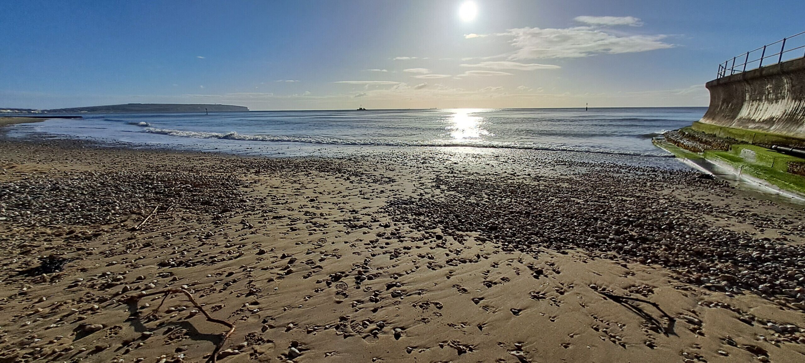 Una playa con huellas en la arena, una barrera de hormigón y el océano al fondo.