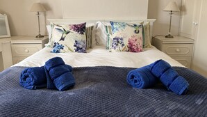 Un letto rifatto con cuscini floreali, due lampade ai comodini e un piccolo specchio tondo appeso al muro.