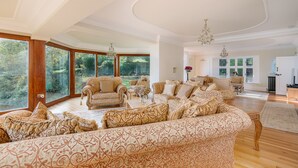 A spacious living room with large windows, a chandelier, and patterned furniture. - Luccombe Chine House (Shanklin)