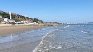 A beach with a pier extending into the water, buildings on a hillside, and a clear sky. - Luccombe Chine House (Shanklin)