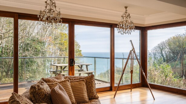 A room with a large window, a wooden floor, a sofa with patterned cushions, and a telescope on a tripod. - Luccombe Chine House (Shanklin)