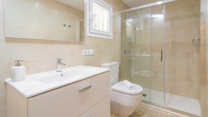 Een moderne badkamer met een wit wastafelmeubel, spiegel en toilet. Er is een douchecabine met glazen wanden.