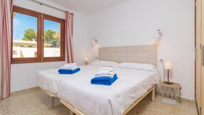 Een tweepersoonsbed met witte en blauwe handdoeken, een nachtkastje met een lamp, en een raam met gordijnen.