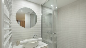 Un bagno moderno con uno specchio rotondo, un lavandino bianco e una cabina doccia in vetro.