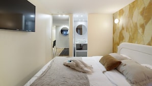 Camera d'albergo con un letto, una TV a parete, un bagno con uno specchio e vista sul corridoio.