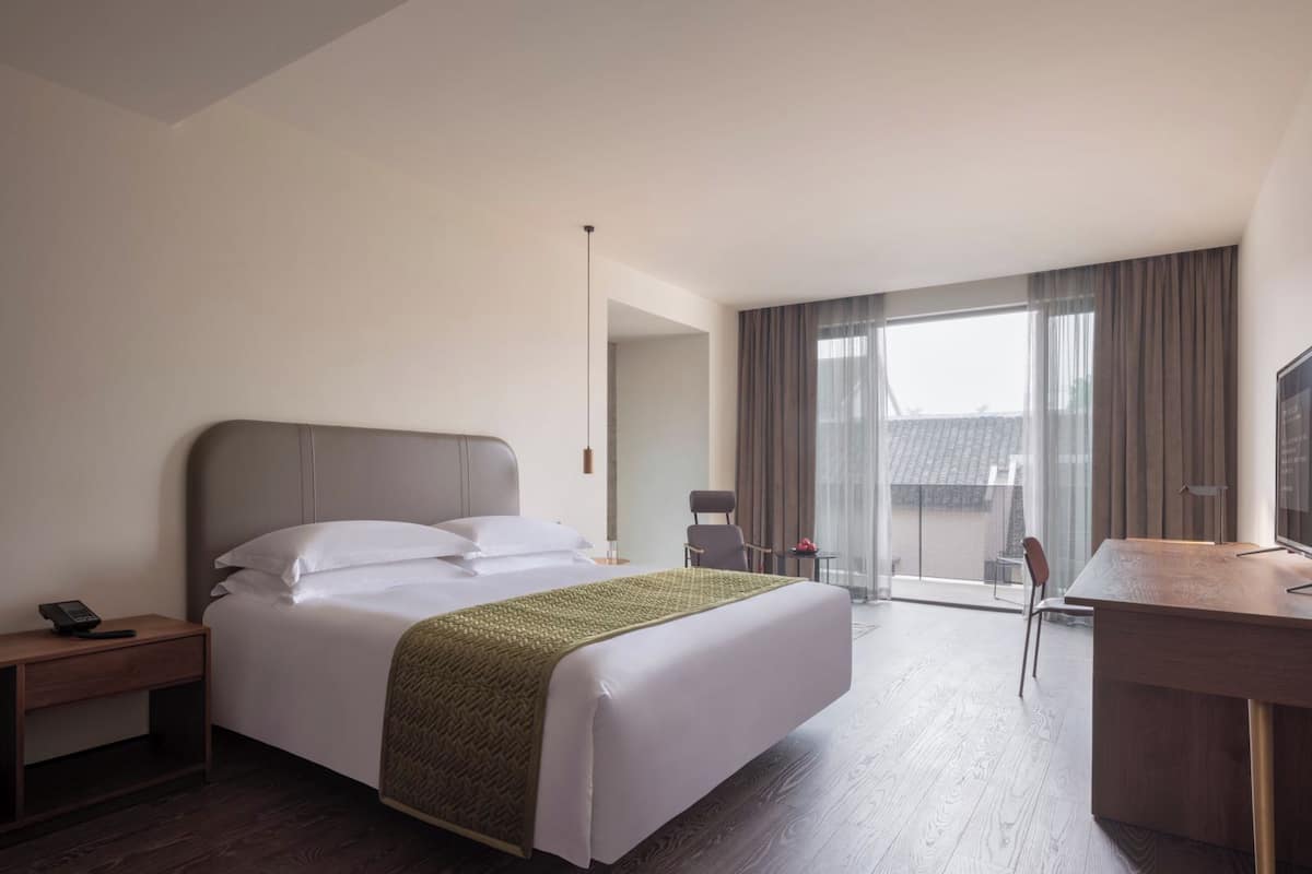 A hotel room with a large bed, a desk, a chair, and a view of the city.