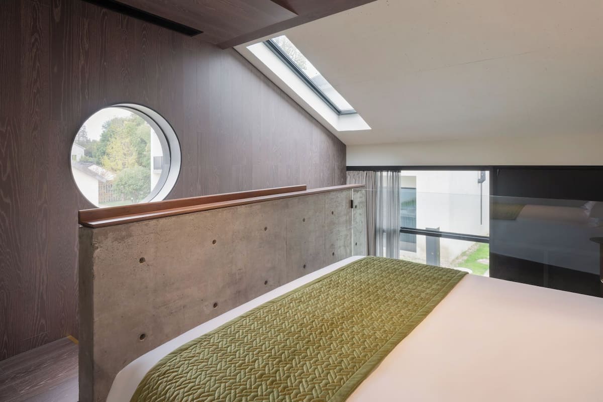A bedroom with a skylight, a round window, and a bed with a green textured bedspread.