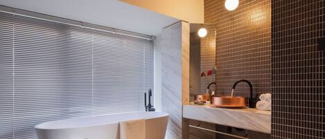 Une salle de bain moderne avec une baignoire sur pieds, un meuble-lavabo avec un vasque en cuivre et un grand miroir.