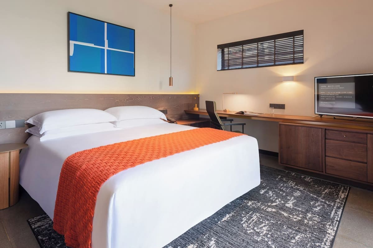 A hotel room with a bed, a desk, a chair, a television, and a window with blinds.