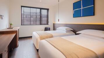 A hotel room with two beds, a desk, a window with blinds, and a blue wall art piece.