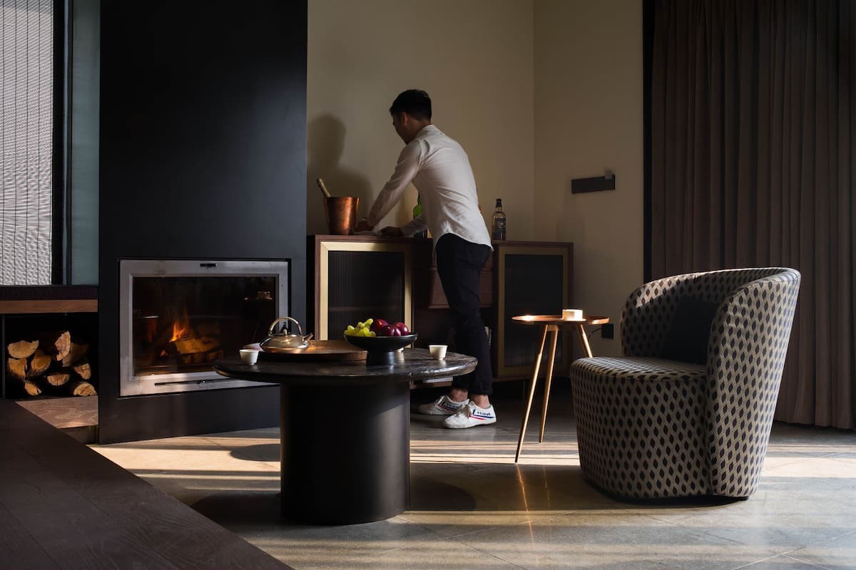 A modern living room with a fireplace, a coffee table with fruits, and a patterned armchair.