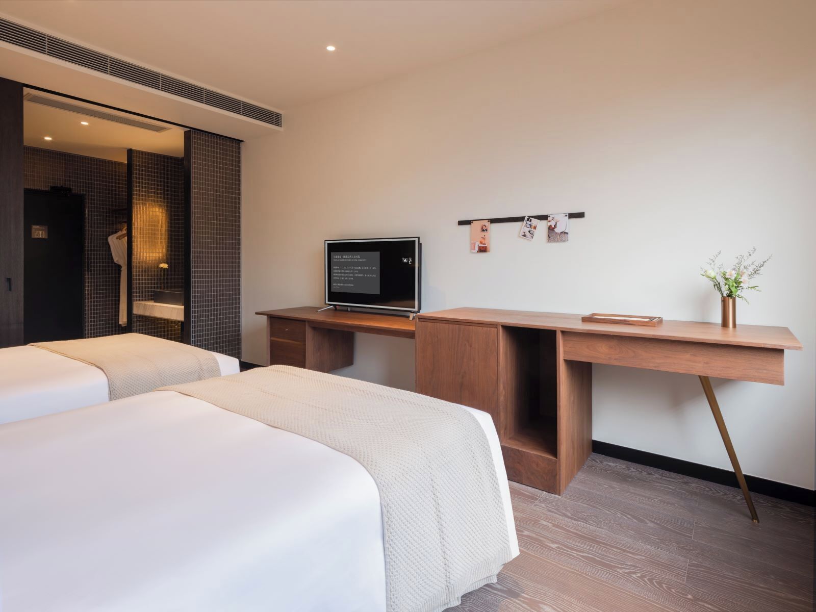 Ett hotellrum med två sängar, ett skrivbord med en dator, en spegel och en liten växt.