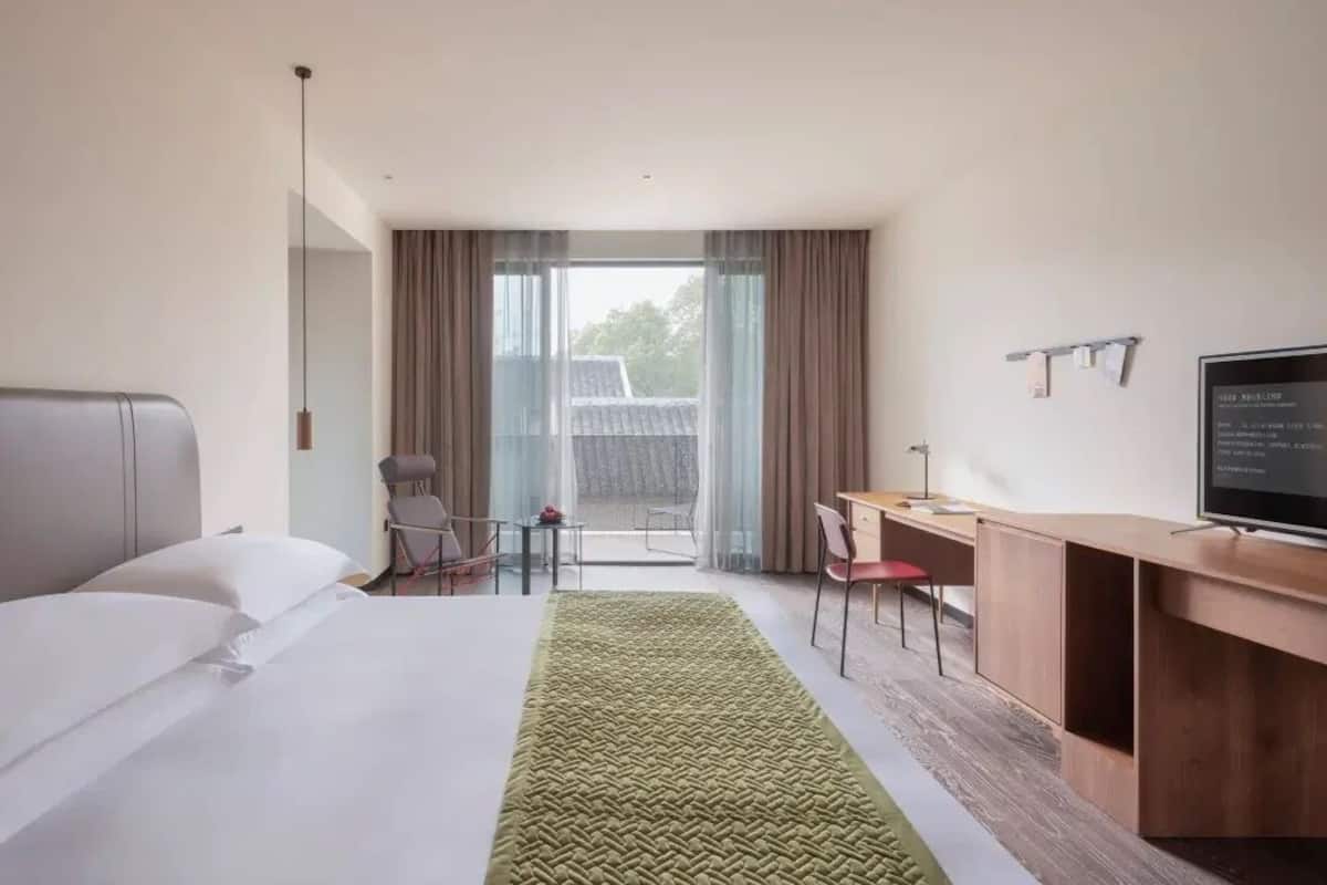 A hotel room with a bed, a desk, a chair, a television, and a view of the outdoors.