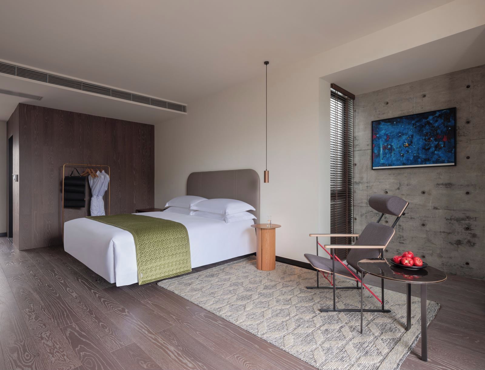 A modern hotel room with a large bed, a seating area with a table, and a painting on the wall.