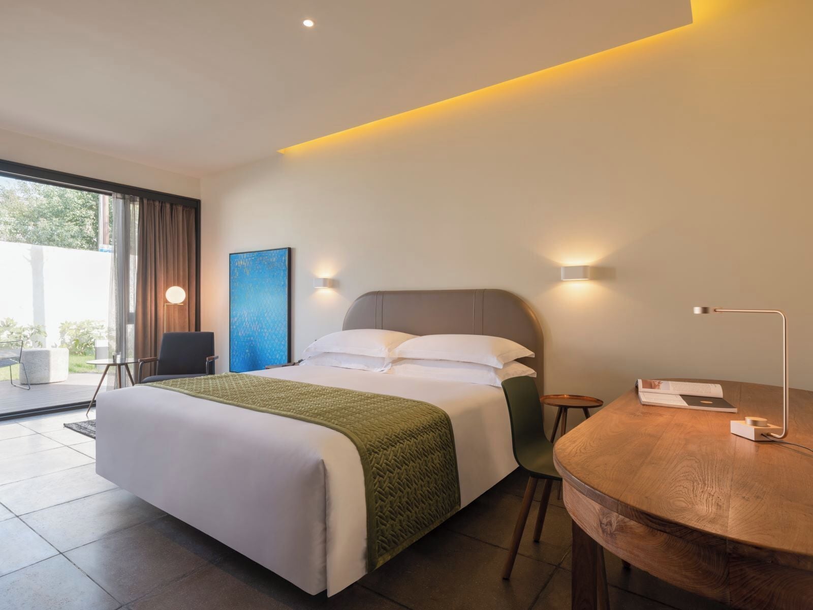Quarto de hotel moderno com uma cama grande, uma mesinha e vista para o exterior.