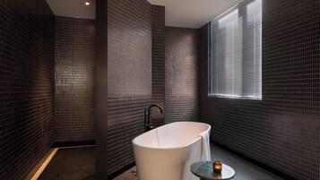 A modern bathroom with a freestanding bathtub, a small round table with a candle, and a window with blinds.