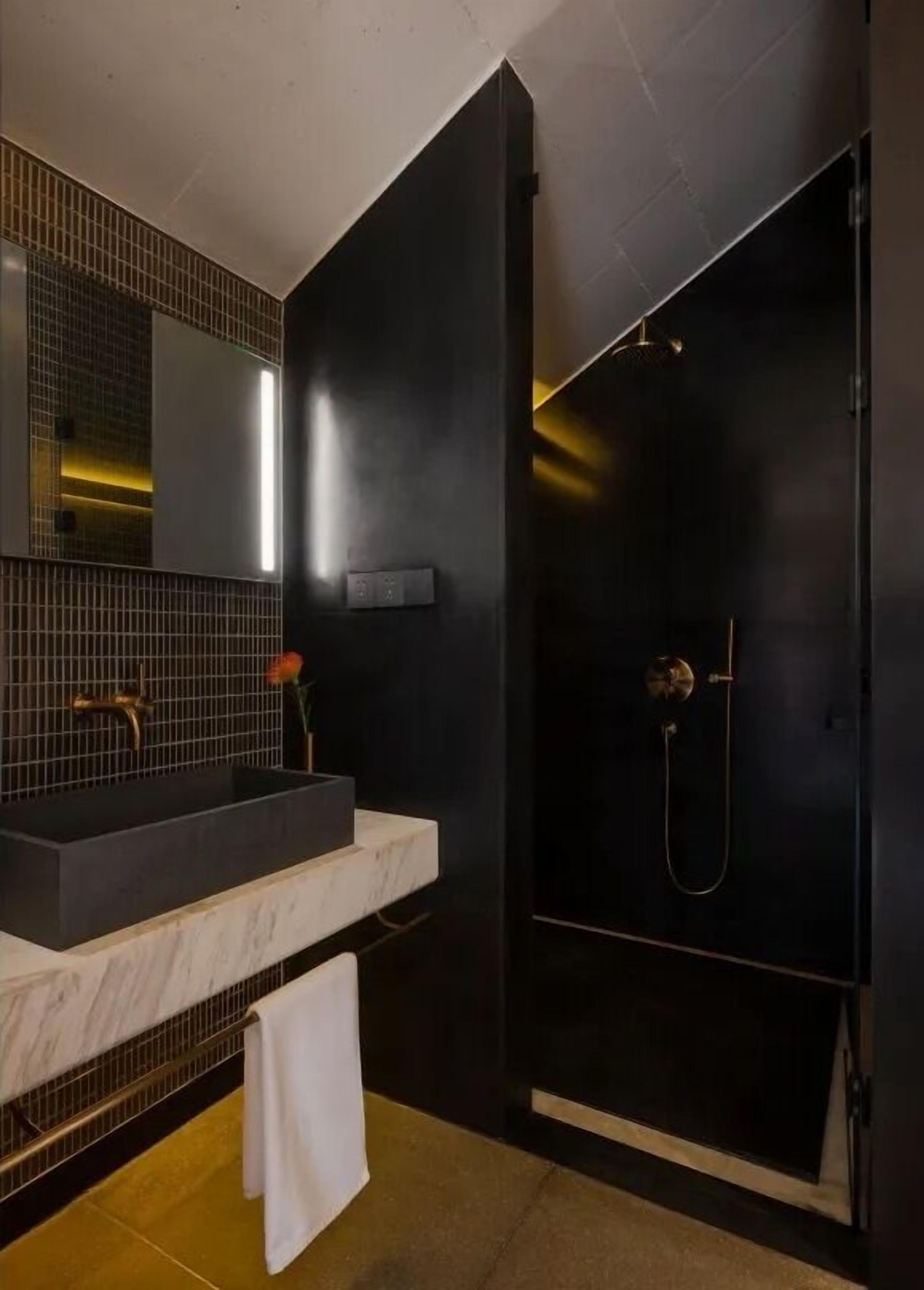 A modern bathroom with a dark theme, featuring a large mirror, a marble countertop, and a black shower enclosure.