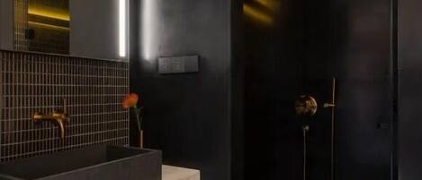 A modern bathroom with a dark theme, featuring a large mirror, a marble countertop, and a black shower enclosure.