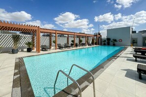 A swimming pool with a wooden pergola, lounge chairs, and potted plants. - Perfect Getaway modern Studio in Luma 22 - JVC (Dubai)