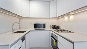 A modern kitchen with white cabinets, a built-in microwave, a gas stove, a sink, and a dishwasher. - Perfect Getaway modern Studio in Luma 22 - JVC (Dubai)