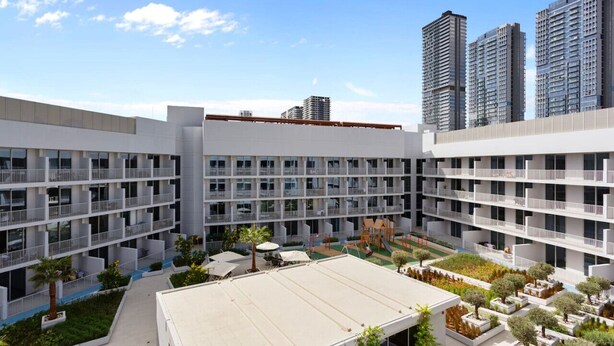 A modern multi-story building with a courtyard featuring outdoor seating, greenery, and a playground. - Perfect Getaway modern Studio in Luma 22 - JVC (Dubai)