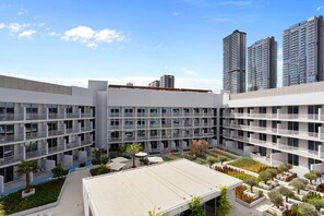 A modern multi-story building with a courtyard featuring outdoor seating, greenery, and a playground.