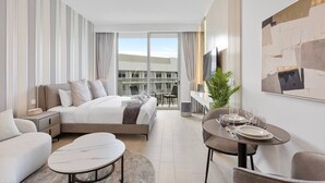 A modern hotel room with a bed, a sitting area with a sofa and coffee table, a dining table set for two, and a large window with curtains. - Perfect Getaway modern Studio in Luma 22 - JVC (Dubai)