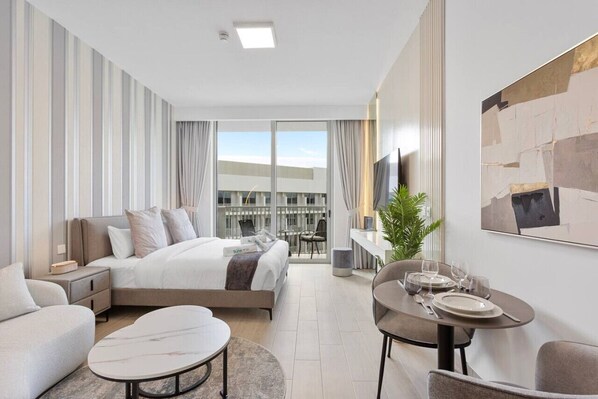 A modern hotel room with a bed, a sitting area with a sofa and coffee table, a dining table set for two, and a large window with curtains.