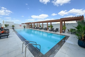 A rooftop pool with lounge chairs and a pergola.