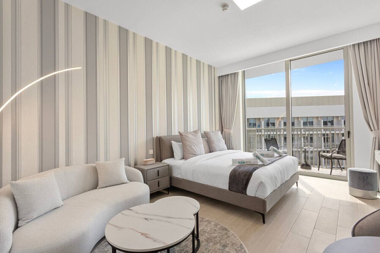 Een moderne hotelkamer met een groot bed, een slaapbank, een klein tafeltje en een balkon met uitzicht op de stad.