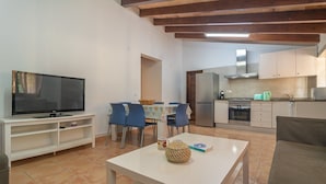 A modern kitchen with white cabinets, a stainless steel range hood, and a dining area with blue chairs and a white table.