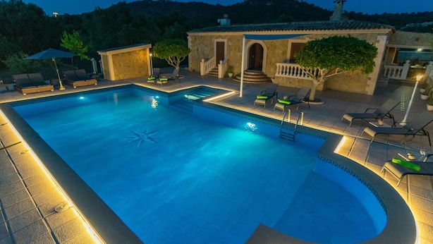 A swimming pool with a sunken center, surrounded by lounge chairs and a small building with steps leading up to it.