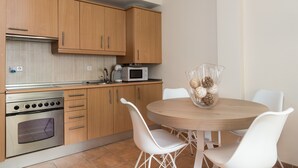 Una cocina moderna con armarios de madera, horno empotrado, microondas y una mesa redonda con sillas blancas.