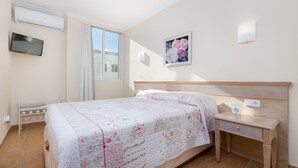 Un dormitorio con cama, mesita de noche y televisor instalado en la pared.