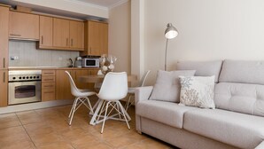 Una cocina moderna con armarios de madera, horno empotrado y comedor con sillas blancas y una mesa.
